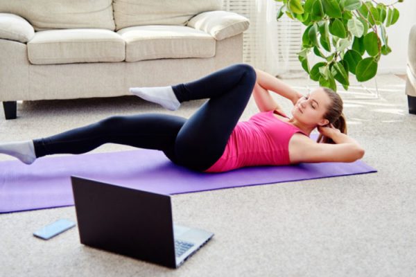 Beautiful young woman doing working out exercise on floor at home, online training on laptop computer, copy space. Yoga, pilates exercising. Sport, healthy lifestyle concept