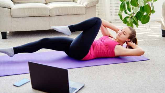 Beautiful young woman doing working out exercise on floor at home, online training on laptop computer, copy space. Yoga, pilates exercising. Sport, healthy lifestyle concept